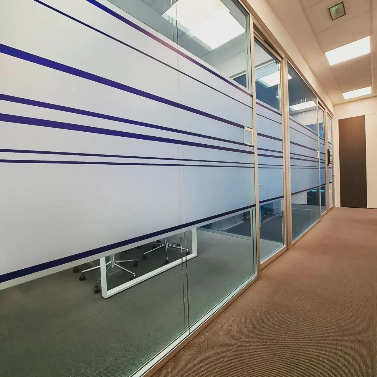 Parete vetrata di un ufficio rivestita con pellicola satinata azzurra e fasce orizzontali